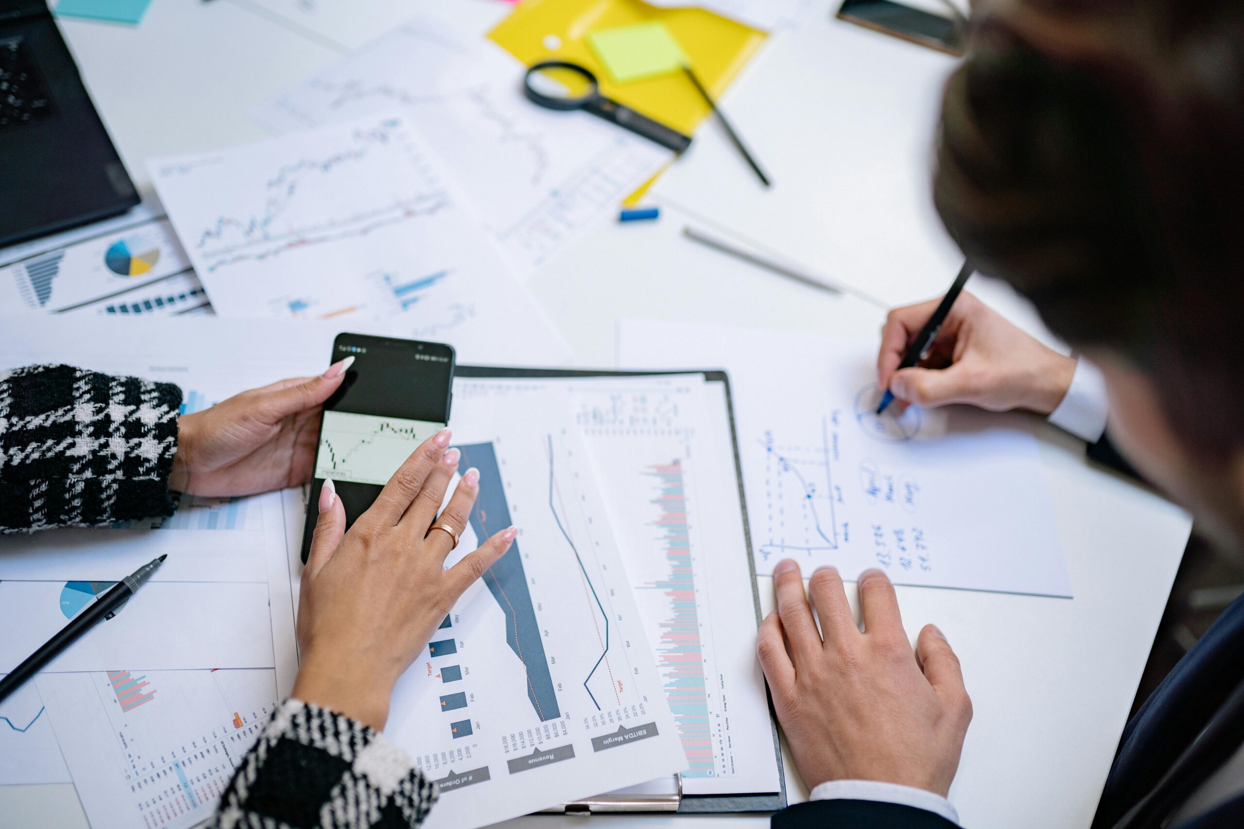 Overhead view of people analyzing financial graphs and data with smartphone and documents.
